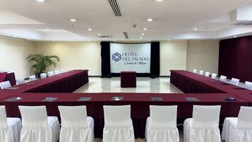 A conference room with a long table, white chairs, and a banner reading "HOTEL DEL PRADO Ciudad de México".