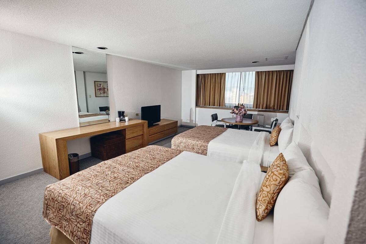 Une chambre d’hôtel avec deux lits, un bureau, une télévision et une fenêtre avec des rideaux.