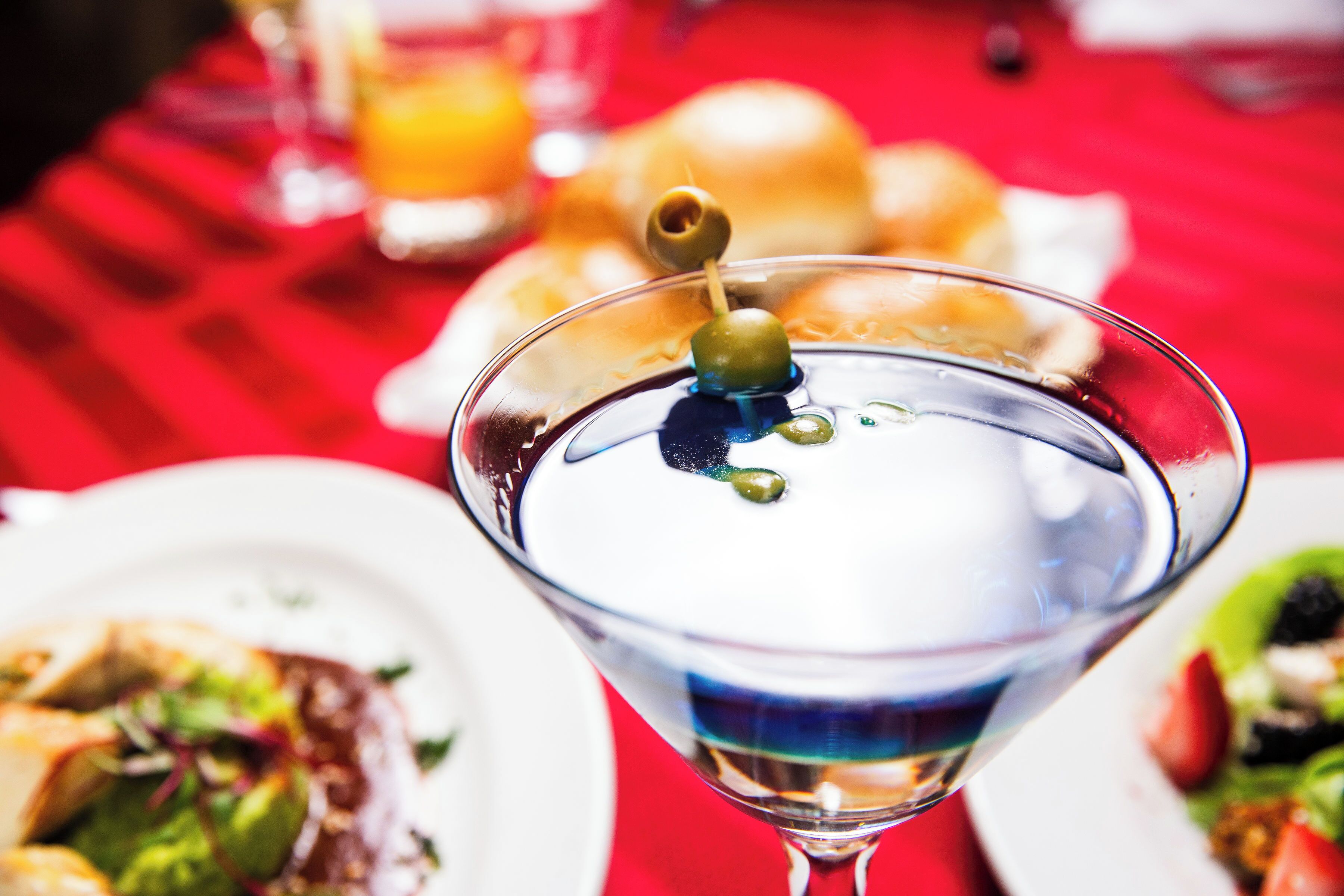 A martini glass with a green olive on a red tablecloth.