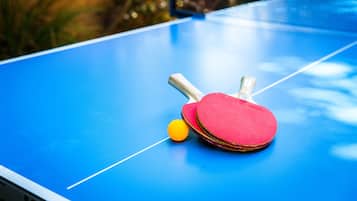 A blue table tennis table with two red paddles and a yellow ball.