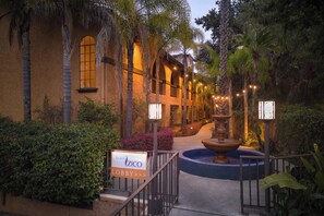 Un hall de hotel con una fuente, palmeras y un letrero que indica el área de recepción.