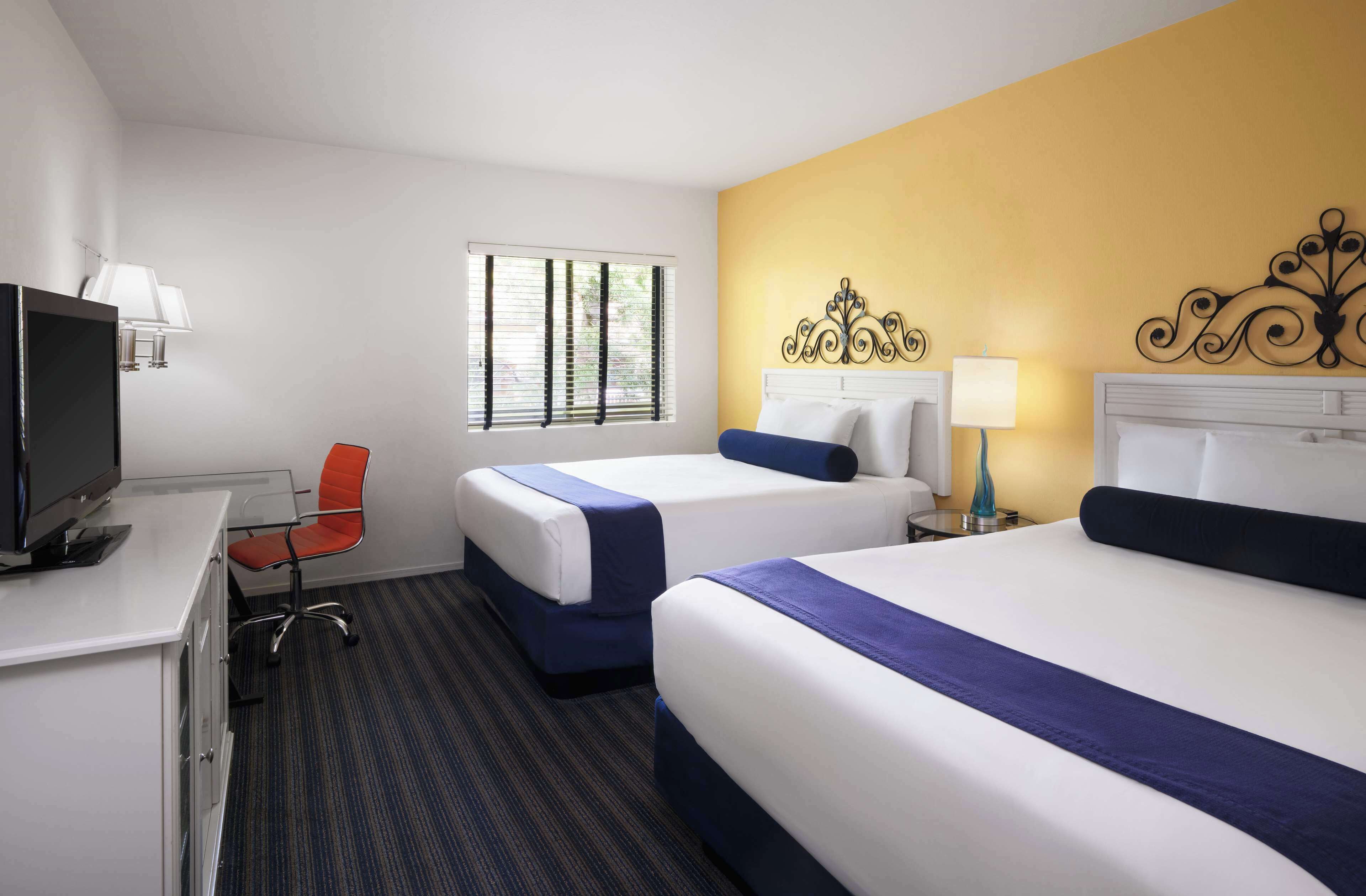 A hotel room with two beds, a desk with a TV, a chair, and a window with blinds.