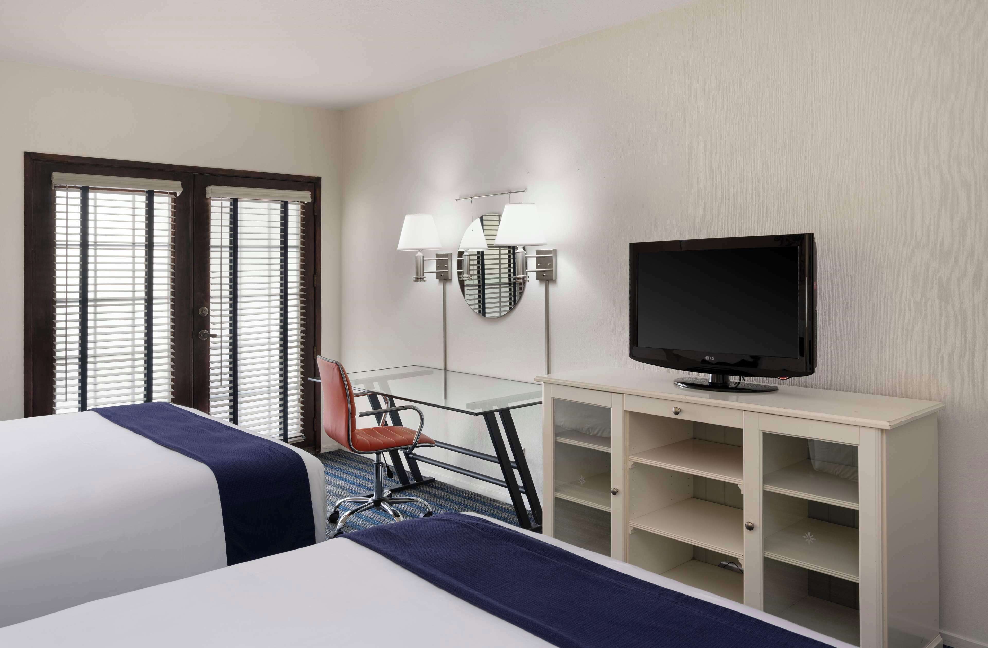Een hotelkamer met twee bedden, een bureau, een stoel, een televisie en een minibar.