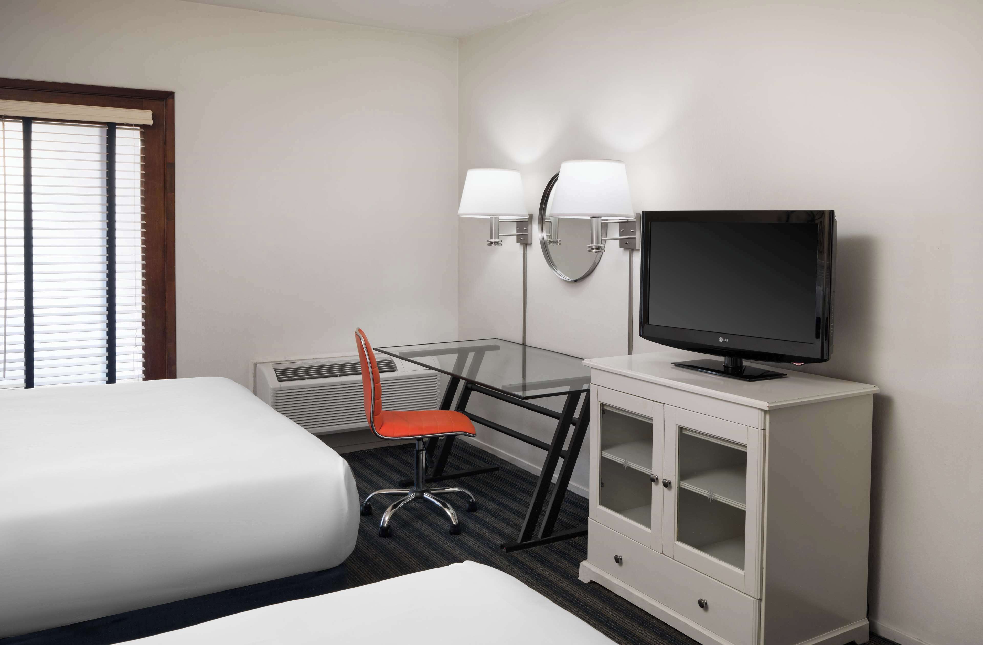 Una habitación de hotel con dos camas, un escritorio con computadora, televisión y una silla.