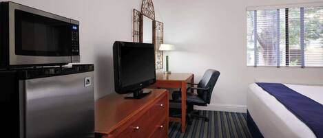 A hotel room with a bed, a desk with a chair, a television, a microwave, and a dresser.