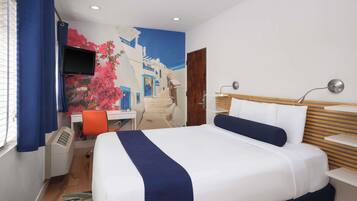 A hotel room with a bed, a desk with a chair, a TV, and a wall mural.