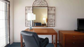Habitación de hotel con un escritorio de madera, una butaca de cuero negro, un televisor sobre una cómoda de madera y un espejo grande con marco de metal decorativo.