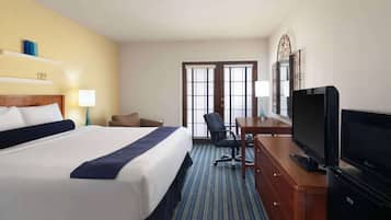 A hotel room with a large bed, a desk with a television, a chair, and a window with blinds.