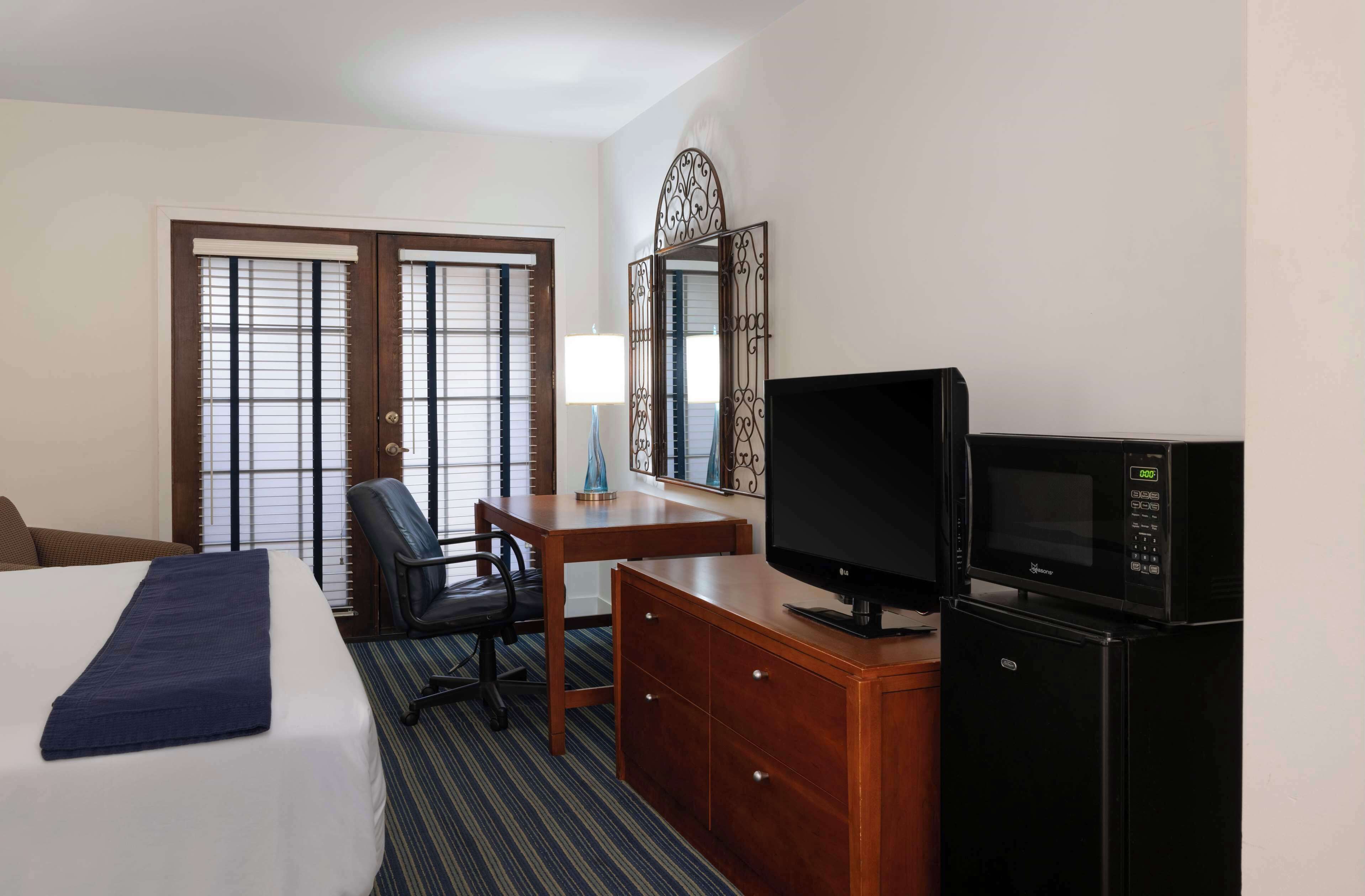 A hotel room with a bed, a desk with a chair, a television, a microwave, and a dresser.