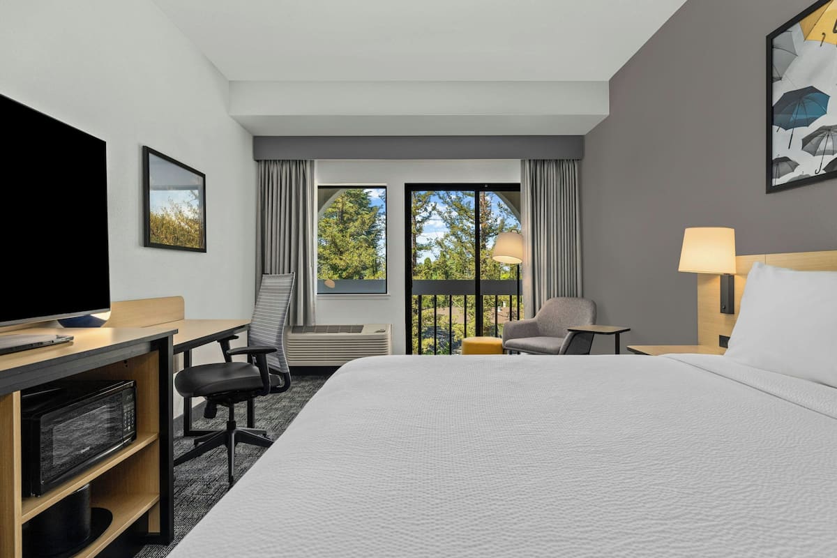 A hotel room with a bed, desk, chair, TV, and a balcony with curtains.