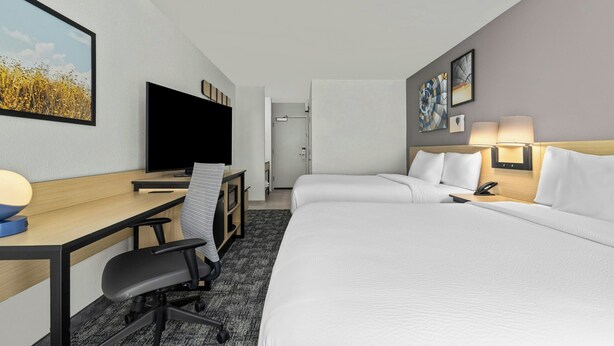A hotel room with a bed, desk, chair, TV, and artwork on the walls.