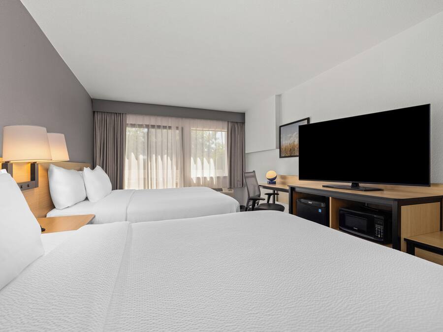 Quarto de hotel com duas camas, uma escrivaninha com computador, televisão e micro-ondas.