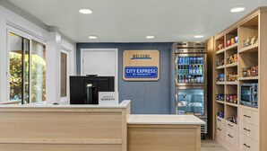 A hotel reception area with a 'City Express by Marriott' sign, a refrigerator stocked with beverages, and a pantry with snacks.