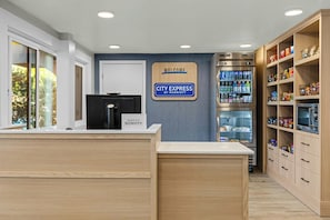 A hotel reception area with a 'City Express by Marriott' sign, a refrigerator stocked with beverages, and a pantry with snacks. - City Express by Marriott Mountain View/Sunnyvale (Mountain View)