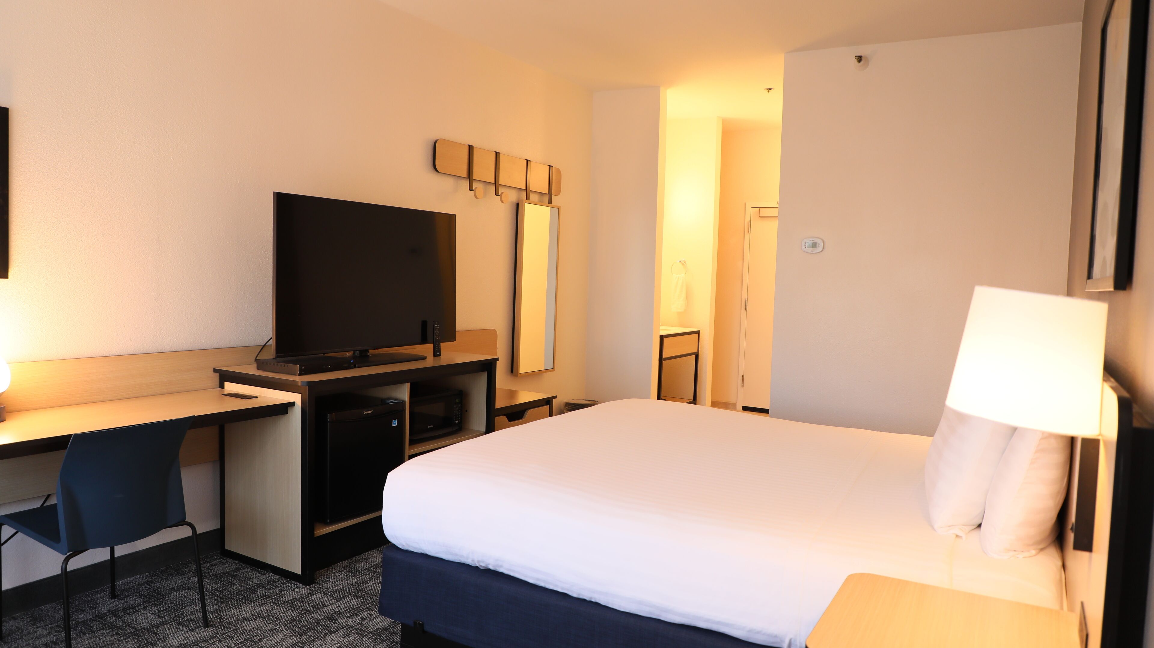 A hotel room with a bed, a desk with a computer, a television, and a mirror.
