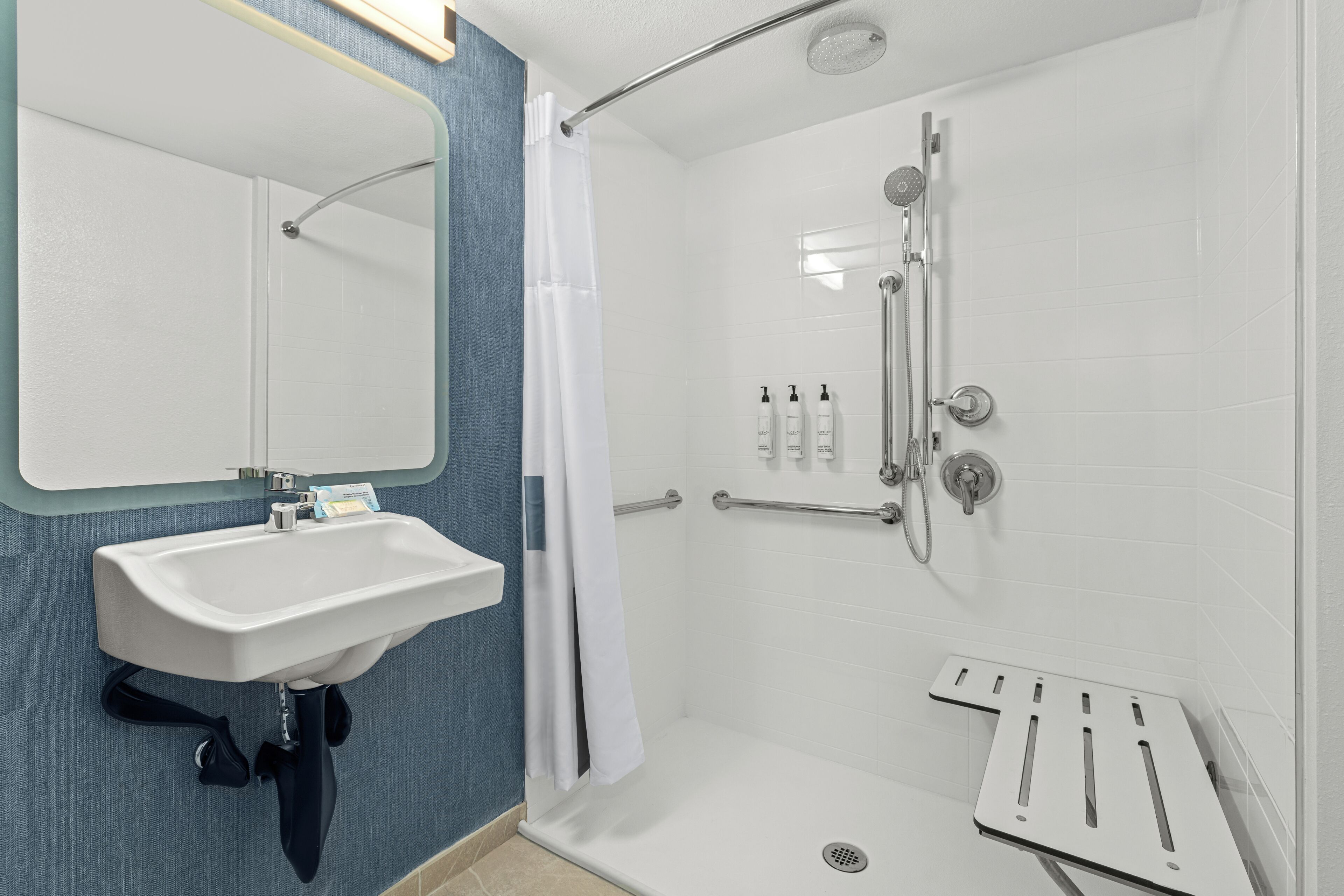 Un baño con lavamanos blanco, espejo, ducha y toallero.