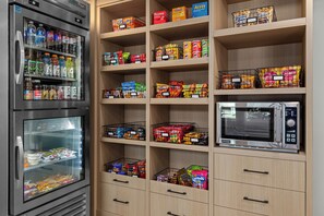 Een kitchenette met een koelkast, magnetron en planken vol snacks en drankjes.