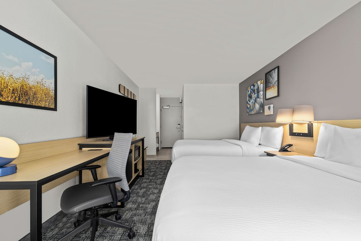 A hotel room with a desk, chair, bed, TV, and artwork on the walls.