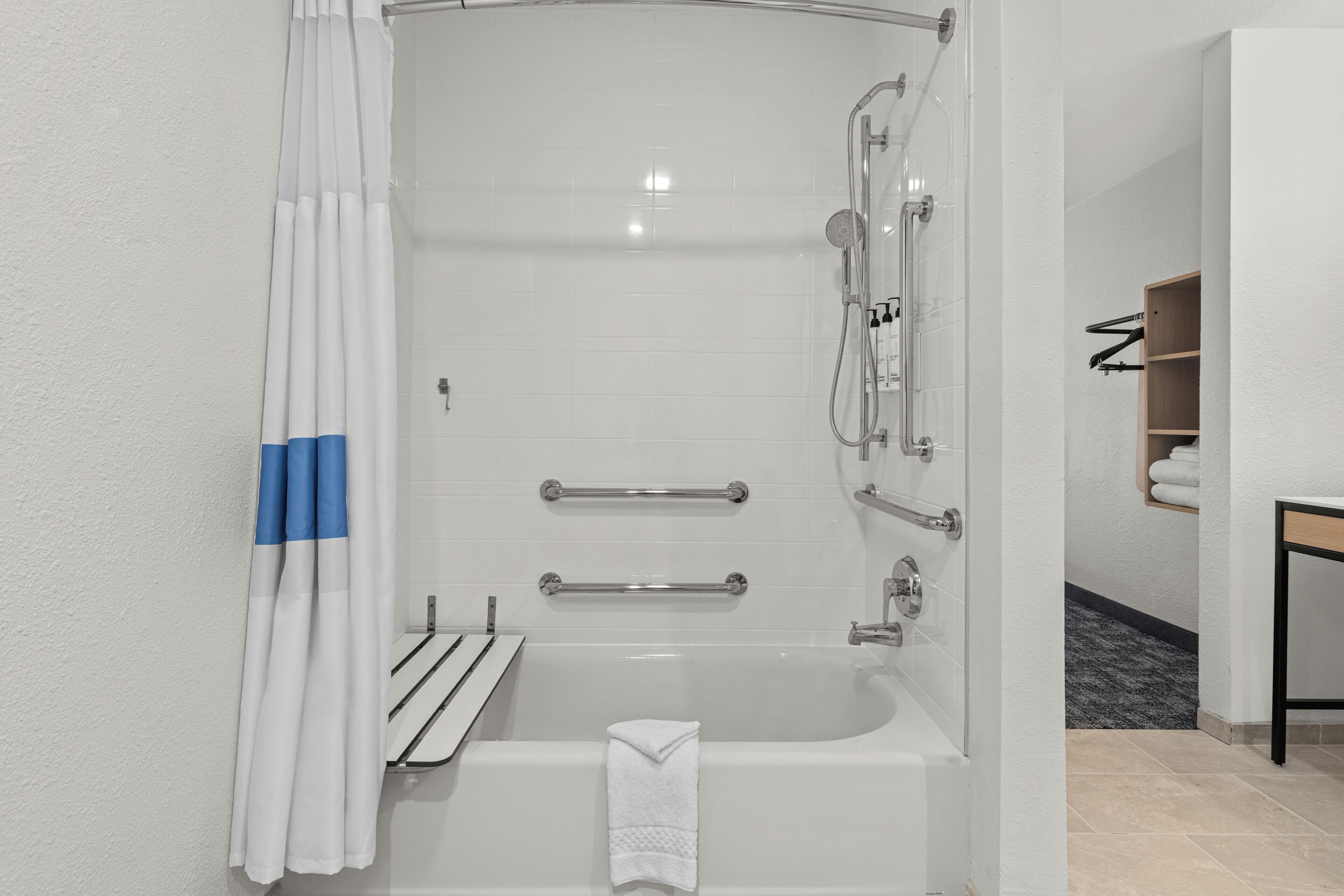 A modern bathroom with a shower, grab bars, a towel rack, and a wooden shelf with towels.