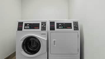 Two stacked front-loading washing machines in a corner with a plain wall and wooden floor.