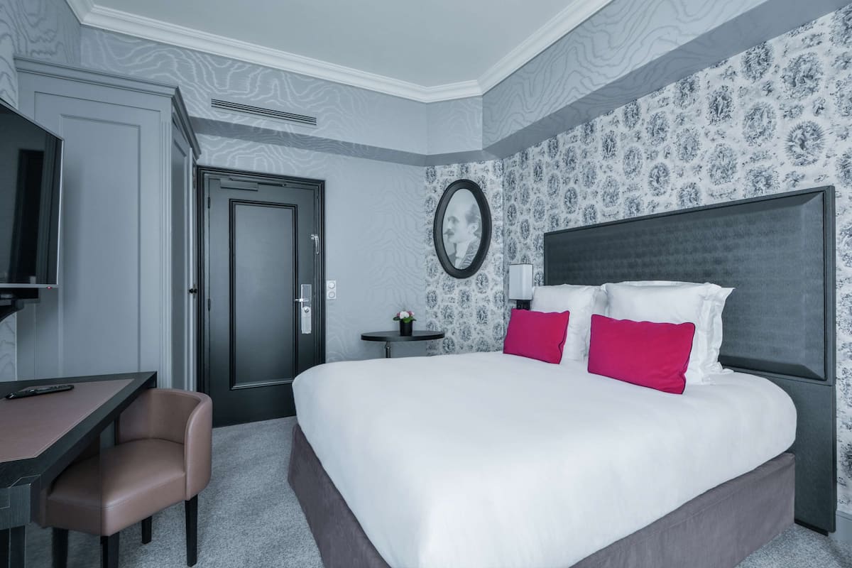 A hotel room with a large bed, a desk, a chair, and a TV.