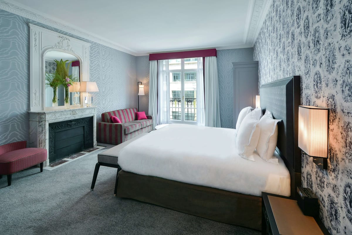 A hotel room with a large bed, a fireplace, a sofa, and a view of the outside.