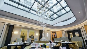 A hotel dining area with a high ceiling and a central chandelier. Tables are set with breakfast items. - Maison Astor Paris, Curio Collection by Hilton (Paris)