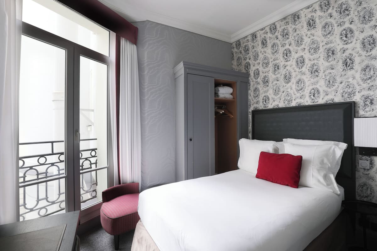 A hotel room with a large bed, a wardrobe, a small seating area, and a balcony with a railing.