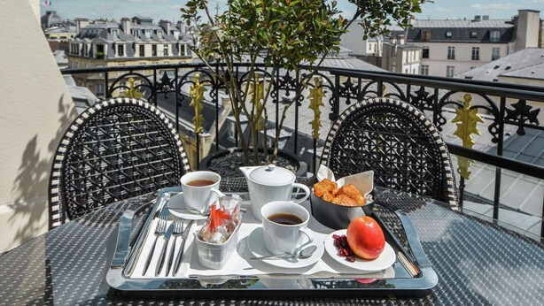 A table set with breakfast items including coffee, croissants, and fruit on a balcony with city views. - Maison Astor Paris, Curio Collection by Hilton (Paris)