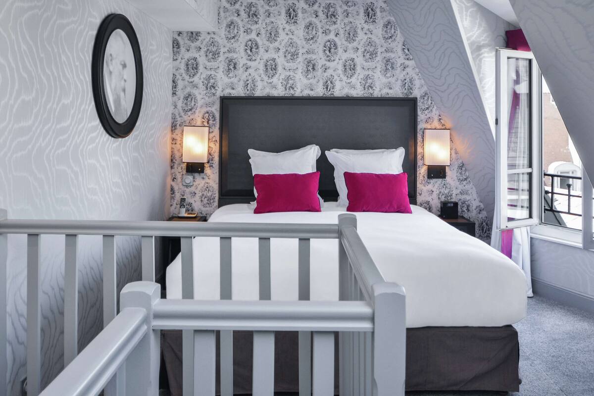 A bedroom with a bed, two bedside lamps, a nightstand, and a window.