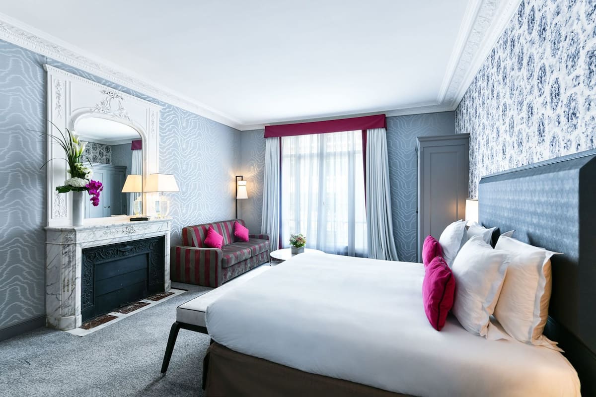 A hotel room with a large bed, a sofa, a fireplace, and a mirror.
