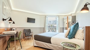 A hotel room with a bed, a desk with a chair, a small table, and a TV on the wall. - Hôtel Petit Lafayette (Paris)