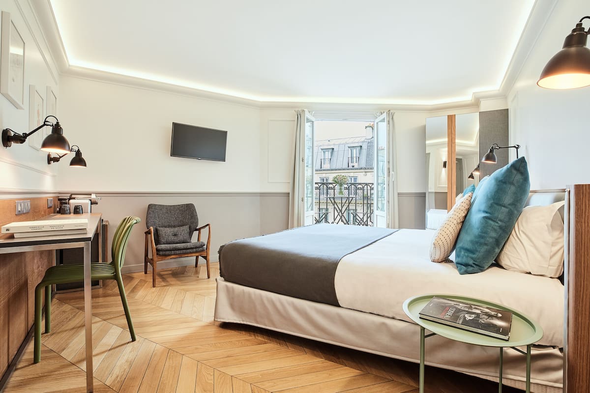 Hotellihuone, jossa on sänky, työpöytä tuolilla, pieni pöytä ja seinälle asennettu televisio.