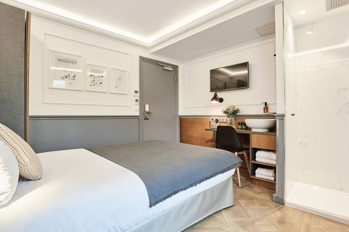 Moderni hotellihuone, jossa on sänky, työpöytä, televisio ja kylpyhuone, jossa on suihku.