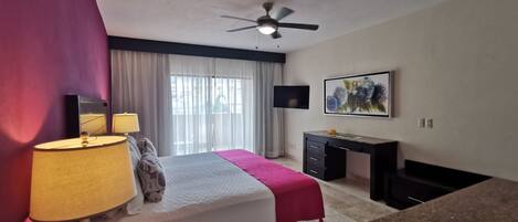 A hotel room with a bed, a desk, a ceiling fan, a TV, and a window with curtains.