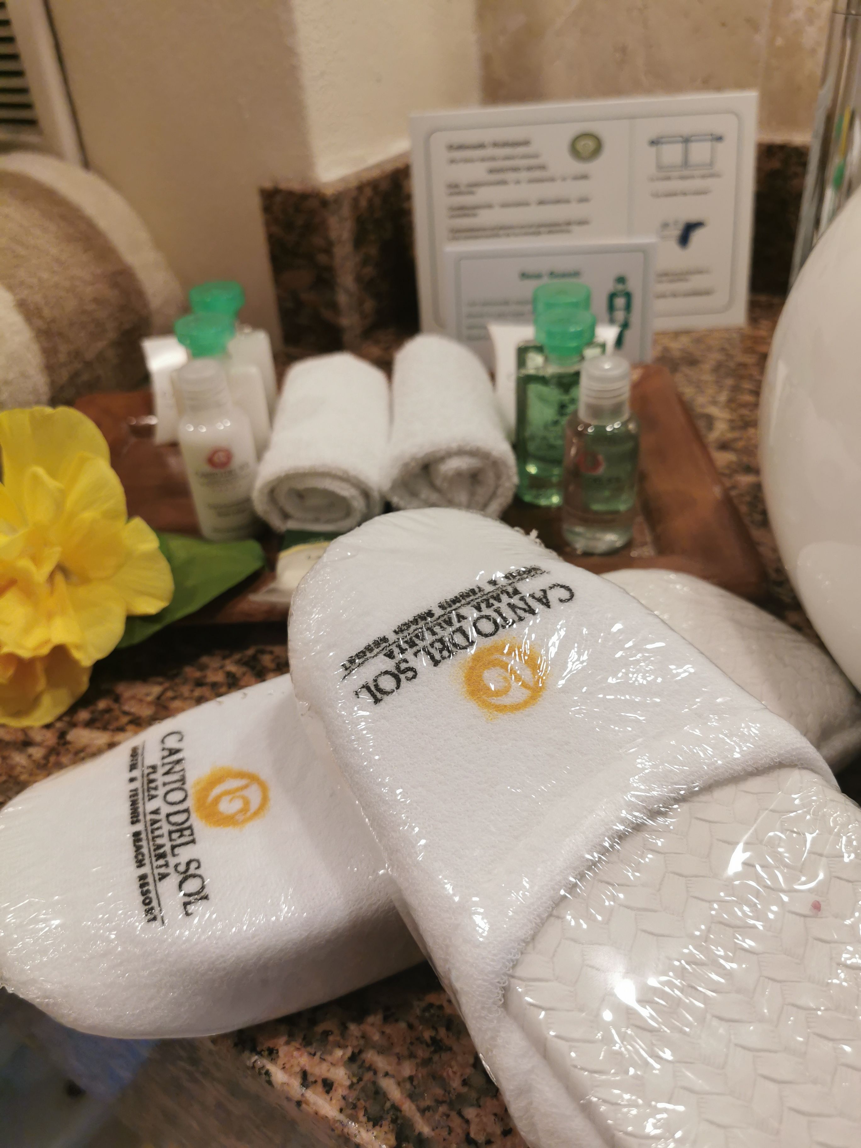 Una encimera de baño con artículos de aseo, toallas y pantuflas.