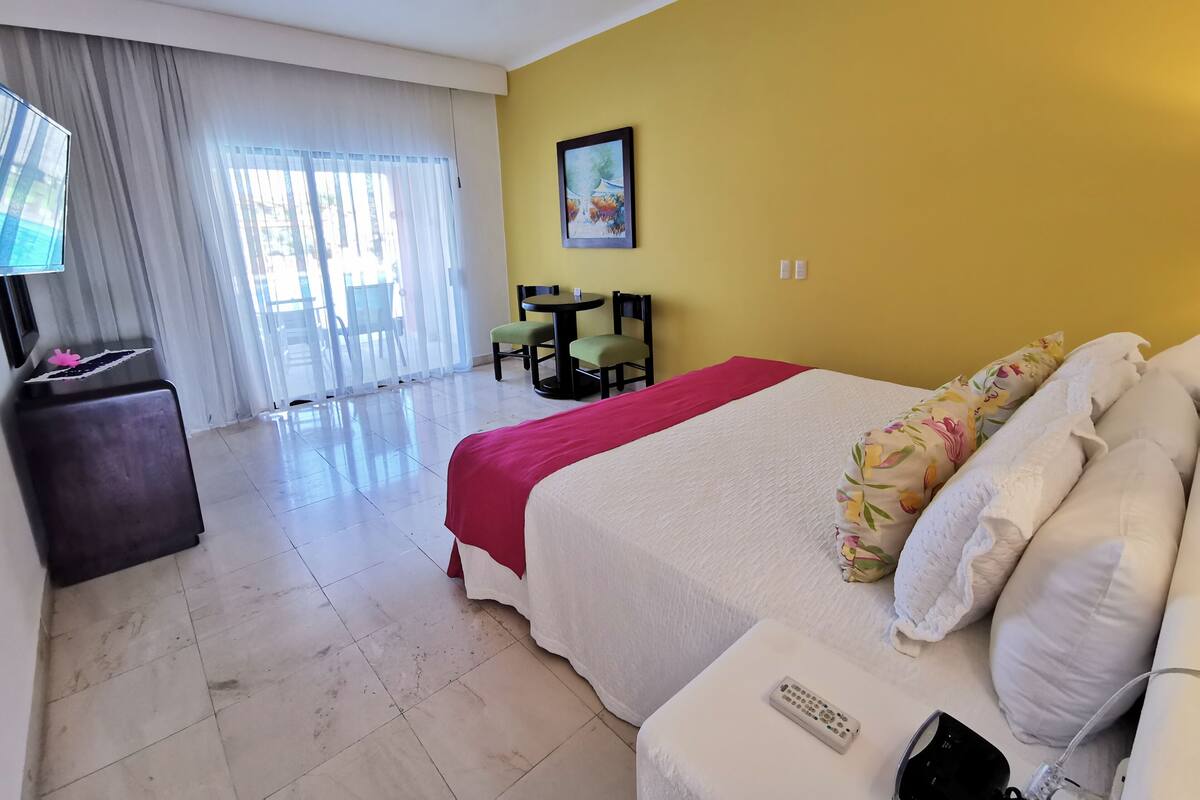 A hotel room with a bed, a desk, a chair, a TV, and a window with curtains.