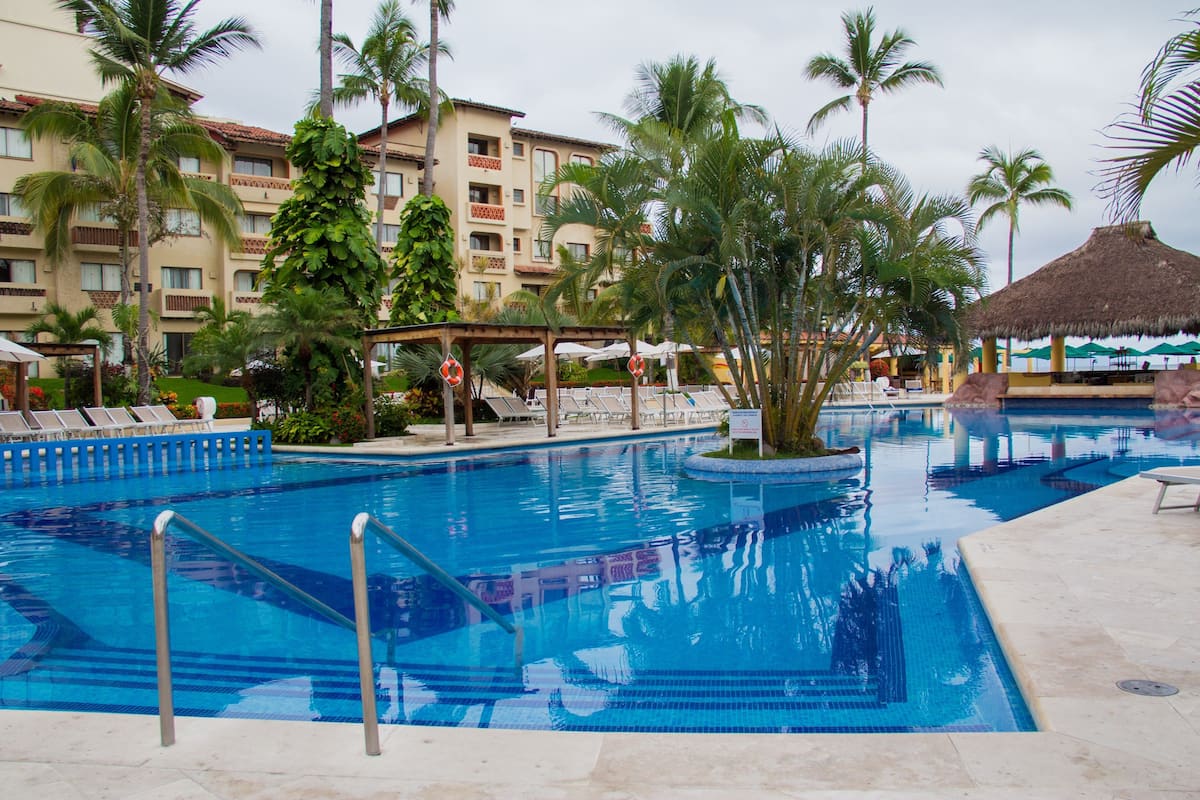 A swimming pool with lounge chairs, palm trees, and a building with balconies in the background.