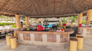 A bar area with a pool in the background, surrounded by lounge chairs and umbrellas. - Canto del Sol Puerto Vallarta All Inclusive (Puerto Vallarta)