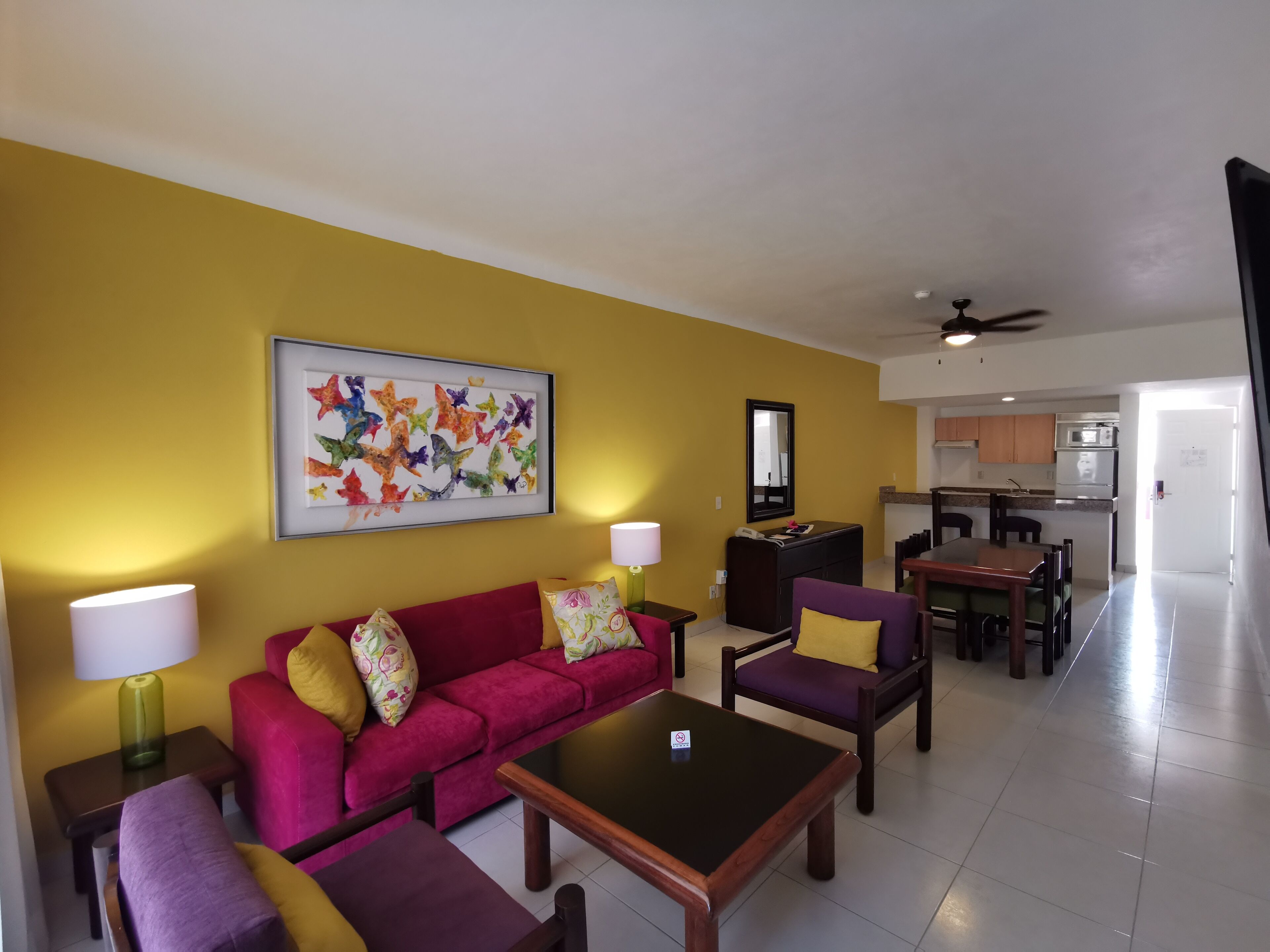 A living room with a sofa, chairs, a coffee table, a dining table, and a kitchen in the background.