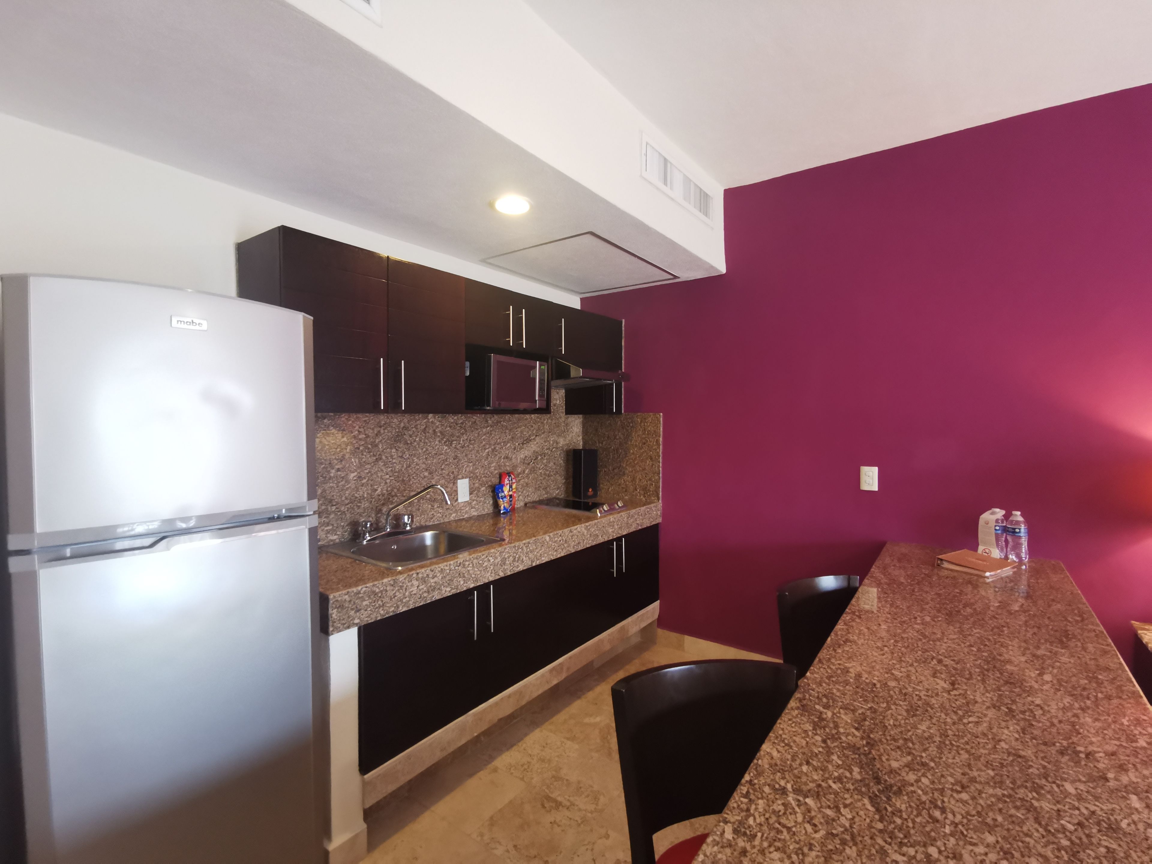 A modern kitchen with a refrigerator, microwave, and granite countertop.