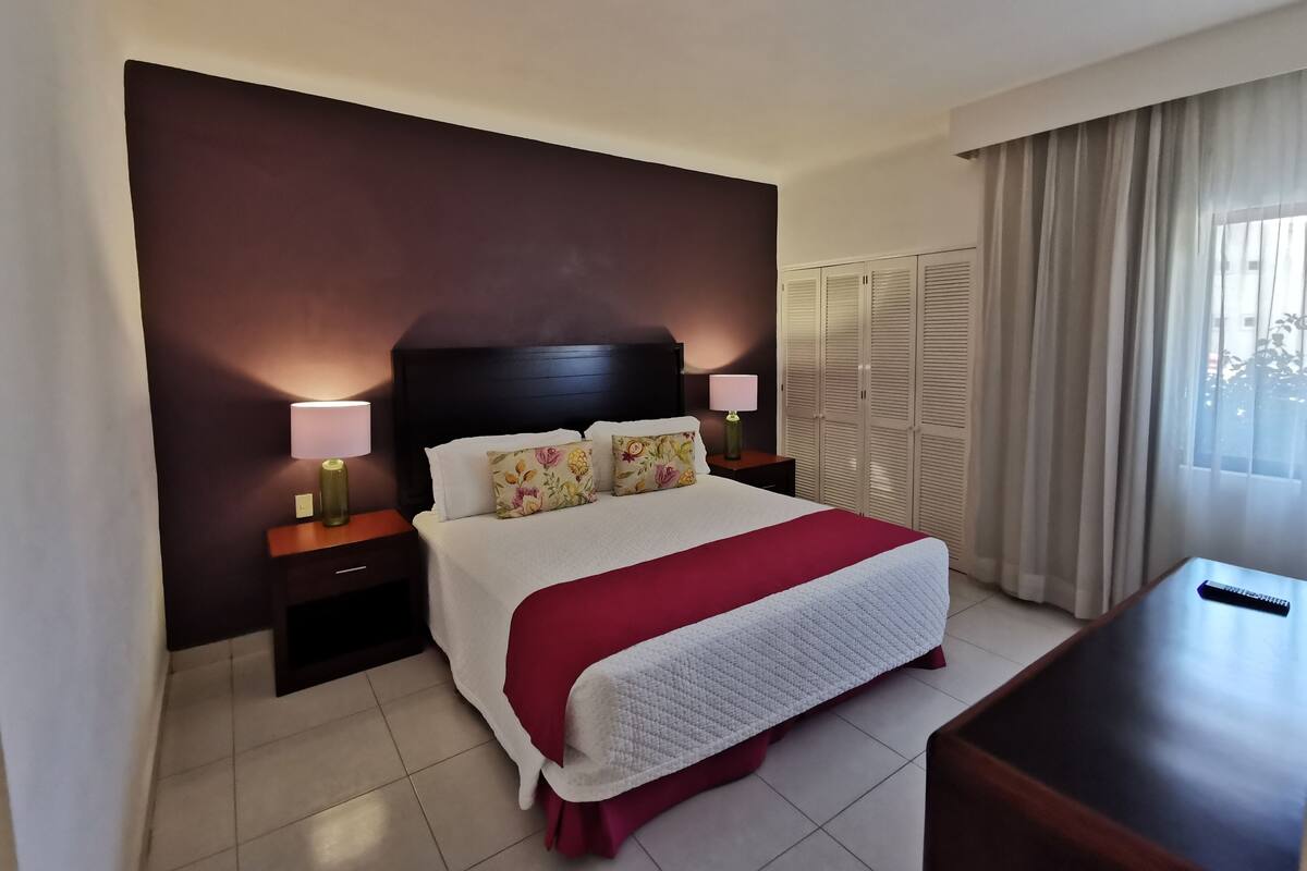 A hotel room with a bed, nightstands, a desk, and a wardrobe.