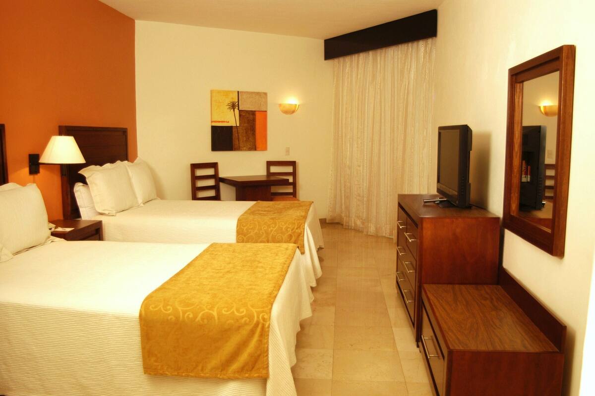 A hotel room with two beds, a desk, a television, and a mirror.