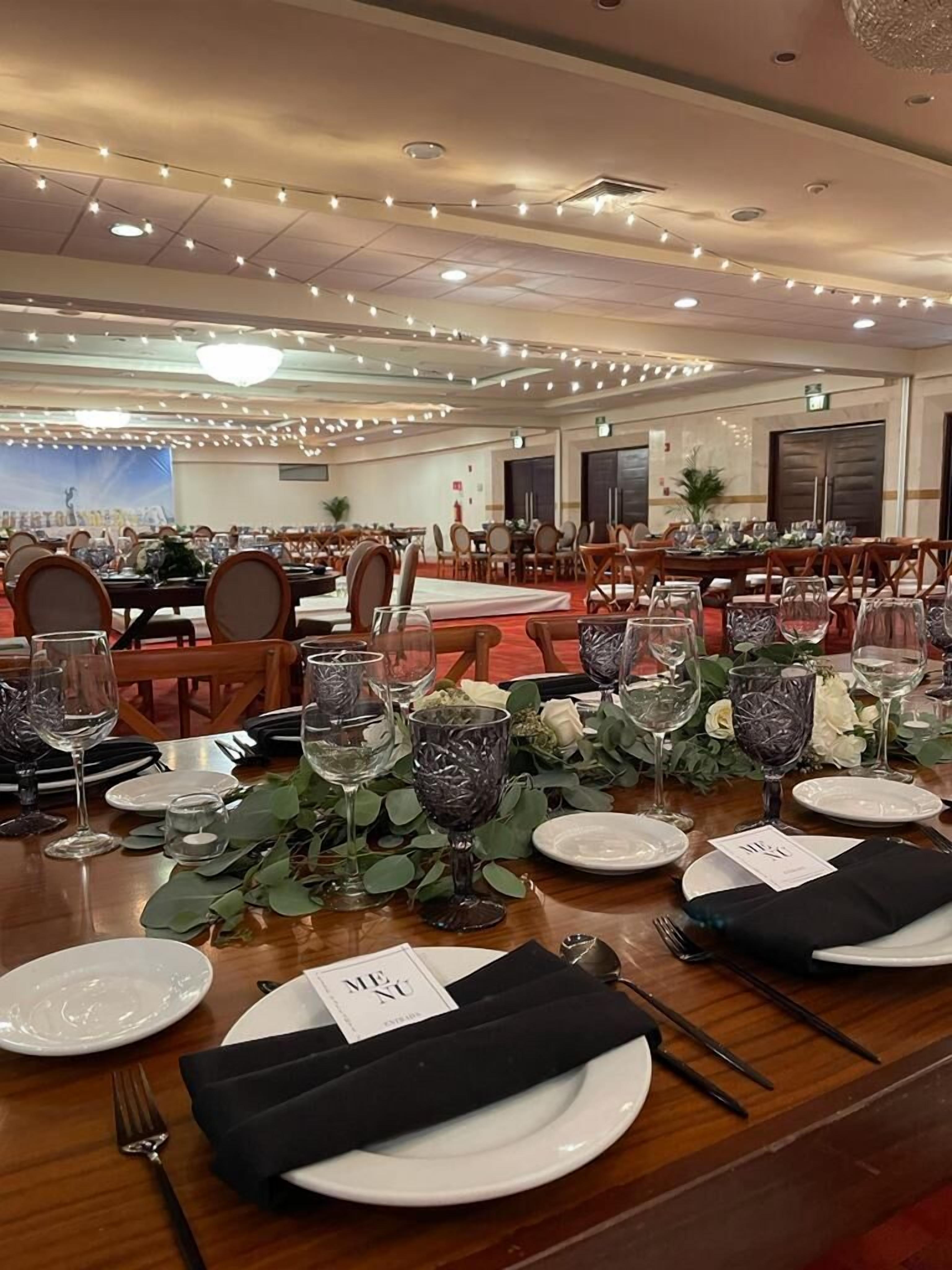 A banquet hall with tables set for a formal event, featuring name cards, glassware, and floral centerpieces.