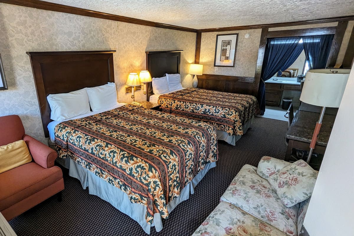Ein Hotelzimmer mit zwei Betten, einem roten Sessel, einem kleinen Tisch und einem Schreibtisch mit einer Lampe.