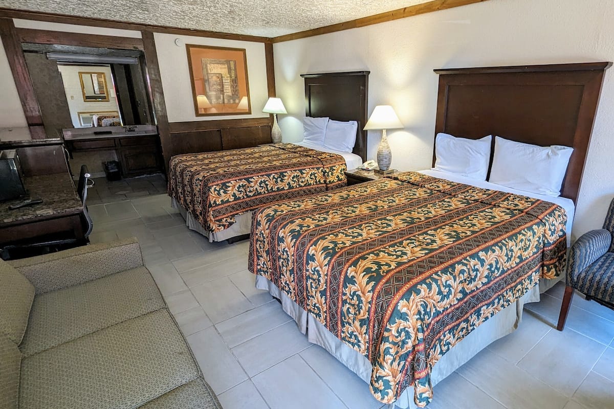 Ein Hotelzimmer mit zwei Betten, einem Schreibtisch, einem Stuhl und einem großen Spiegel.