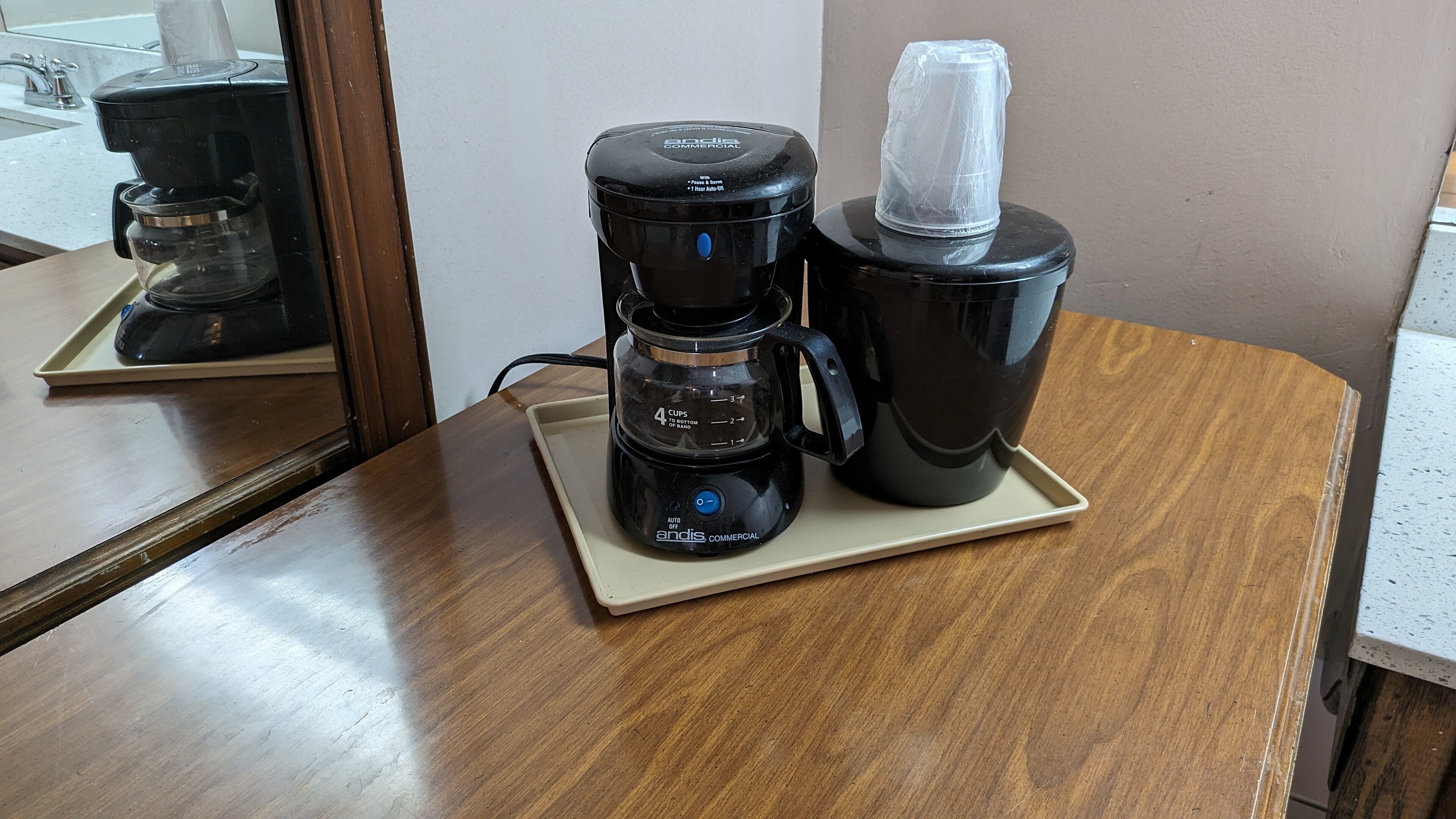 A coffee maker on a wooden table with a mirror reflecting the room.