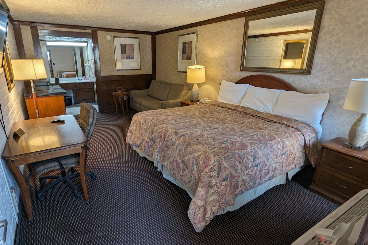 Ein Hotelzimmer mit Bett, Nachttischen, Schreibtisch, Stuhl, Spiegel und Fernseher.