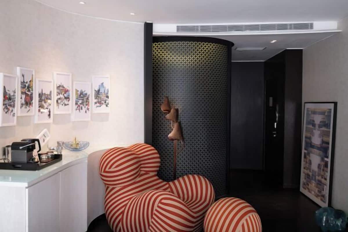 A room with a curved wall, a unique striped chair, a lamp, and framed pictures on the wall.