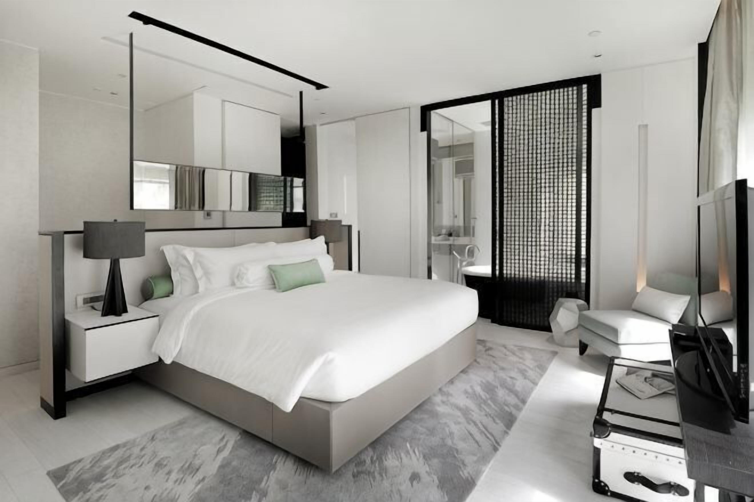 A modern bedroom with a large bed, bedside tables, a TV, and a bathroom visible through an open door.